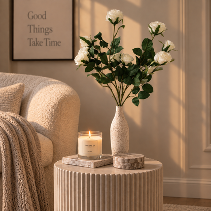 White rose stems with green leaves in speckled beige vase on round table