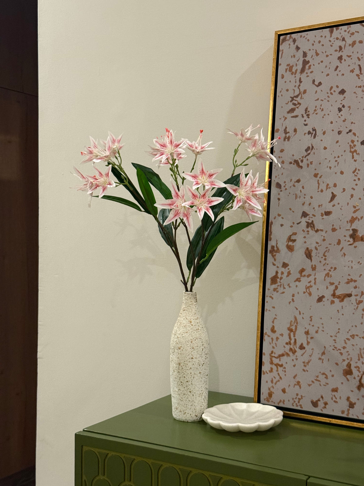 Pink star-shaped flower stems with green leaves in a speckled ceramic vase