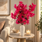Hot pink bougainvillea stems in a tall speckled white vase with dark green leaves