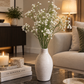 White blossom stems in a ribbed beige ceramic vase on a tabletop